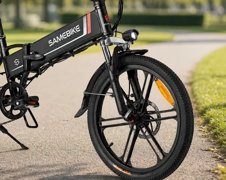 Two folding electric bikes, a Samebike 20LVXD30-II and a Samebike CY20, parked side by side outside a UK station.